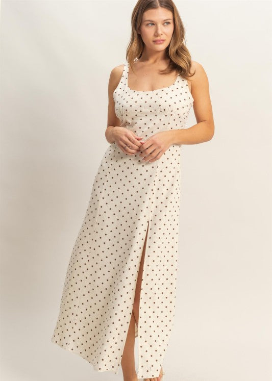 Woman wearing a white polka dot dress with a slit on a plain background