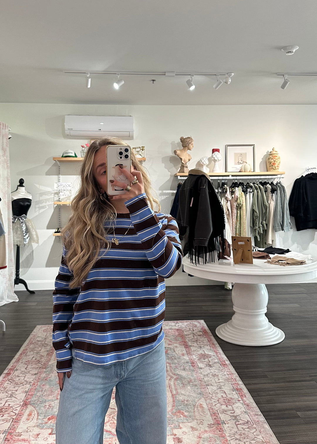 Person taking a mirror selfie in a clothing store wearing a striped sweater and jeans.