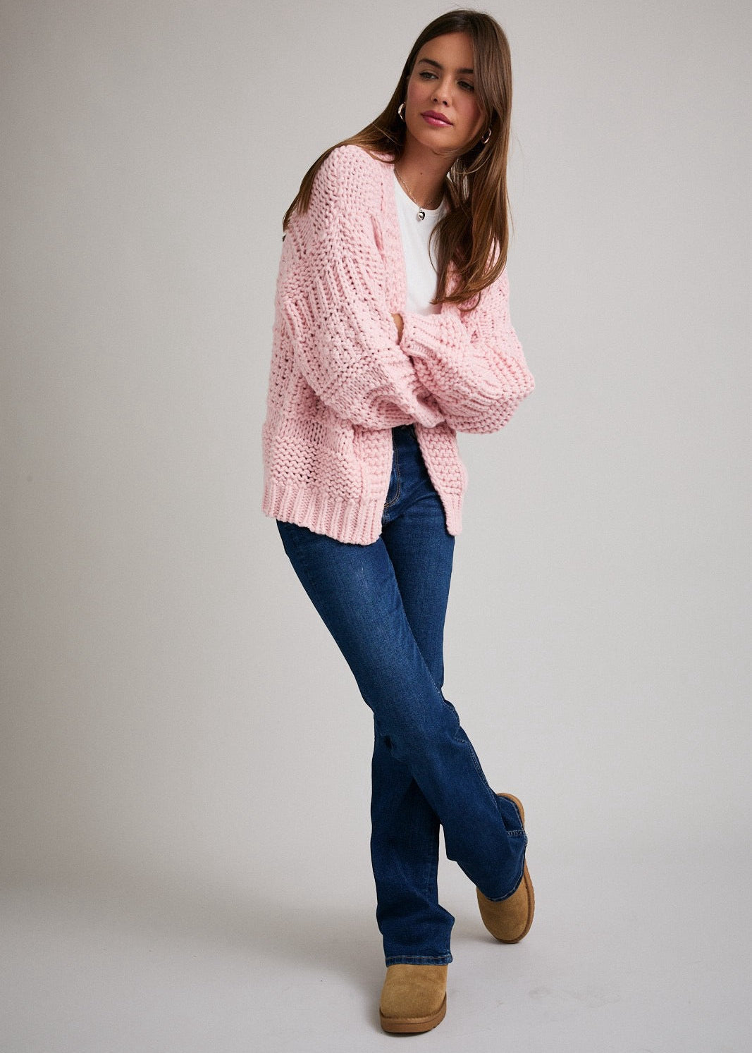 Woman wearing a pink knitted sweater and blue jeans on a plain background