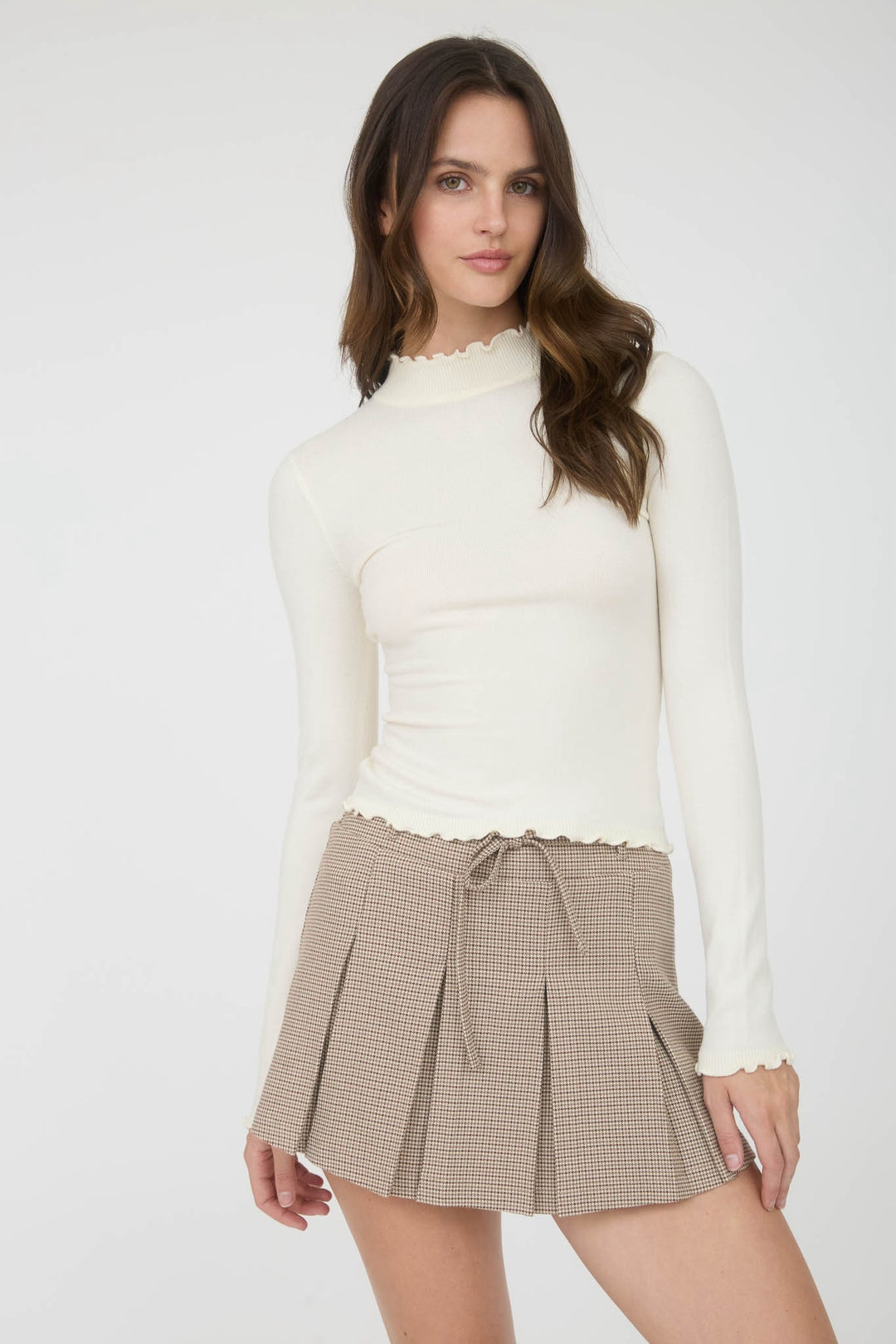 Woman wearing a white long-sleeve top and a brown checkered skirt on a white background