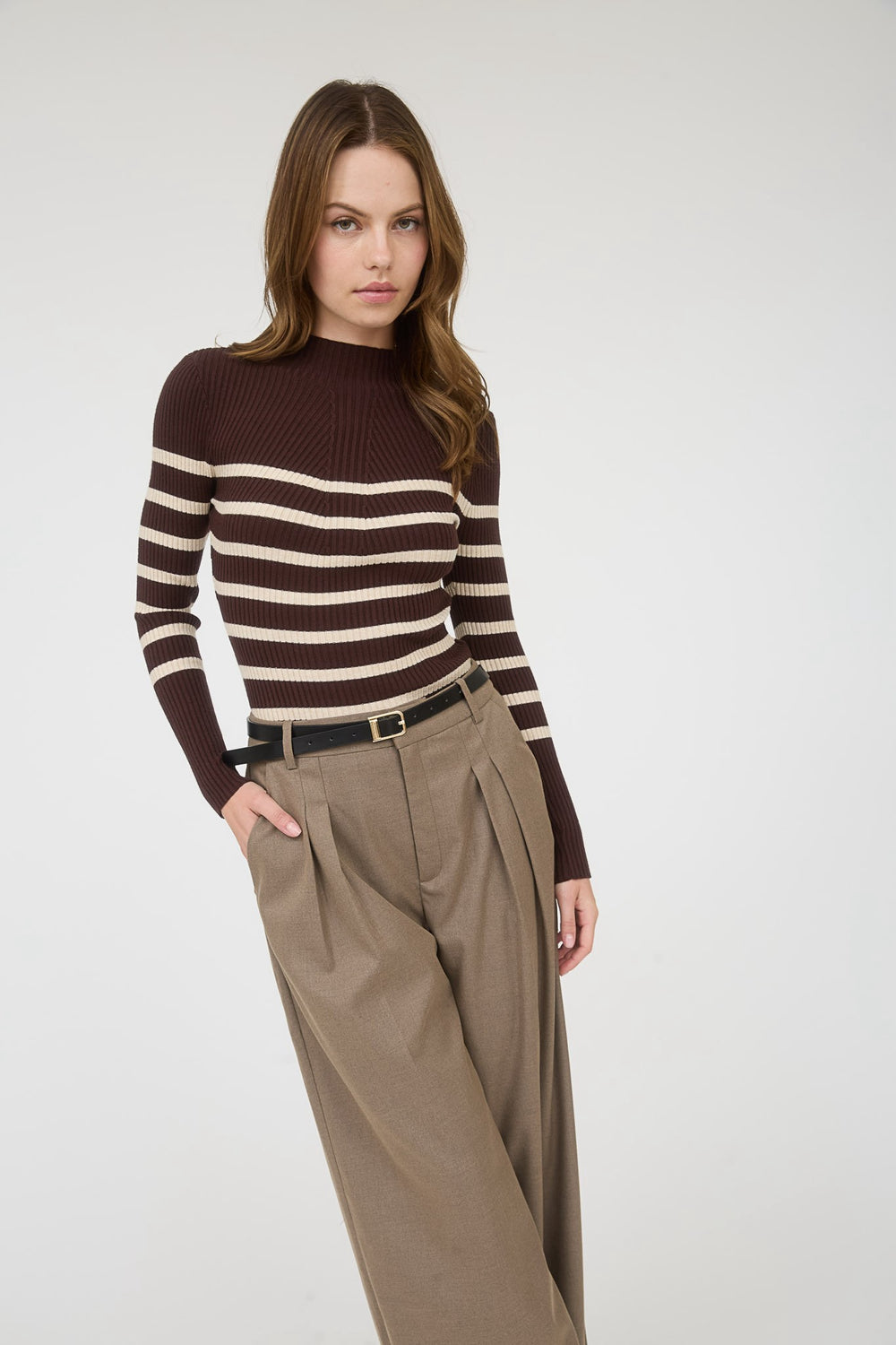 Woman wearing a brown and white striped sweater with beige pants on a white background