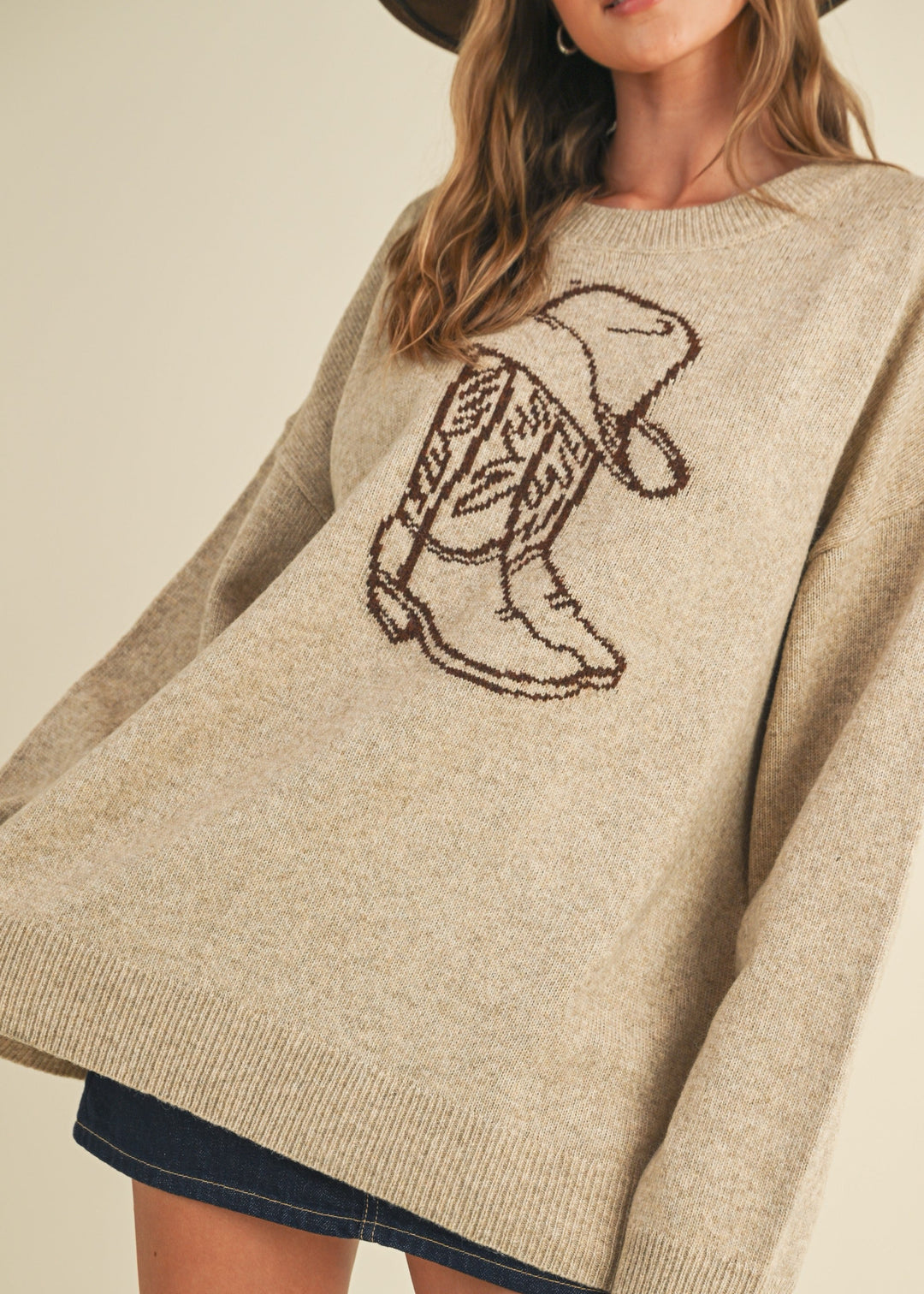 Beige sweater with embroidered design worn by a person on a beige background