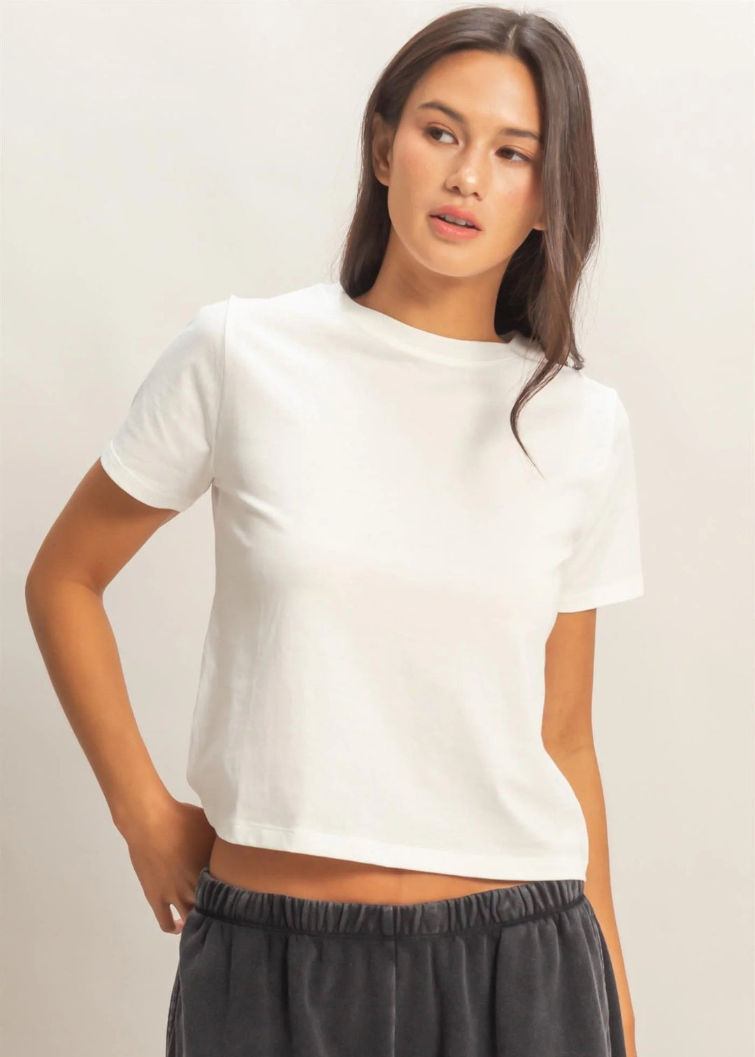 Woman wearing a white t-shirt and dark pants against a plain background