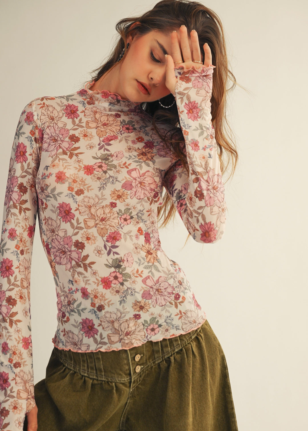 Woman wearing a floral long-sleeve top and green pants against a plain background