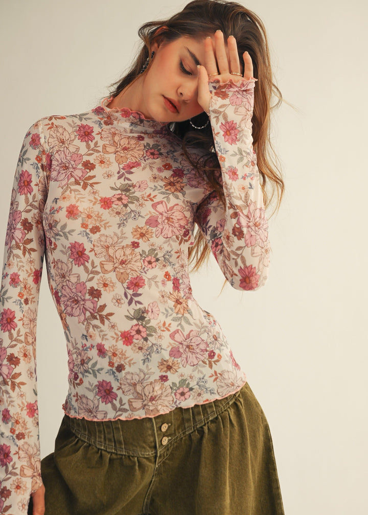 Woman wearing a floral long-sleeve top and green pants against a plain background
