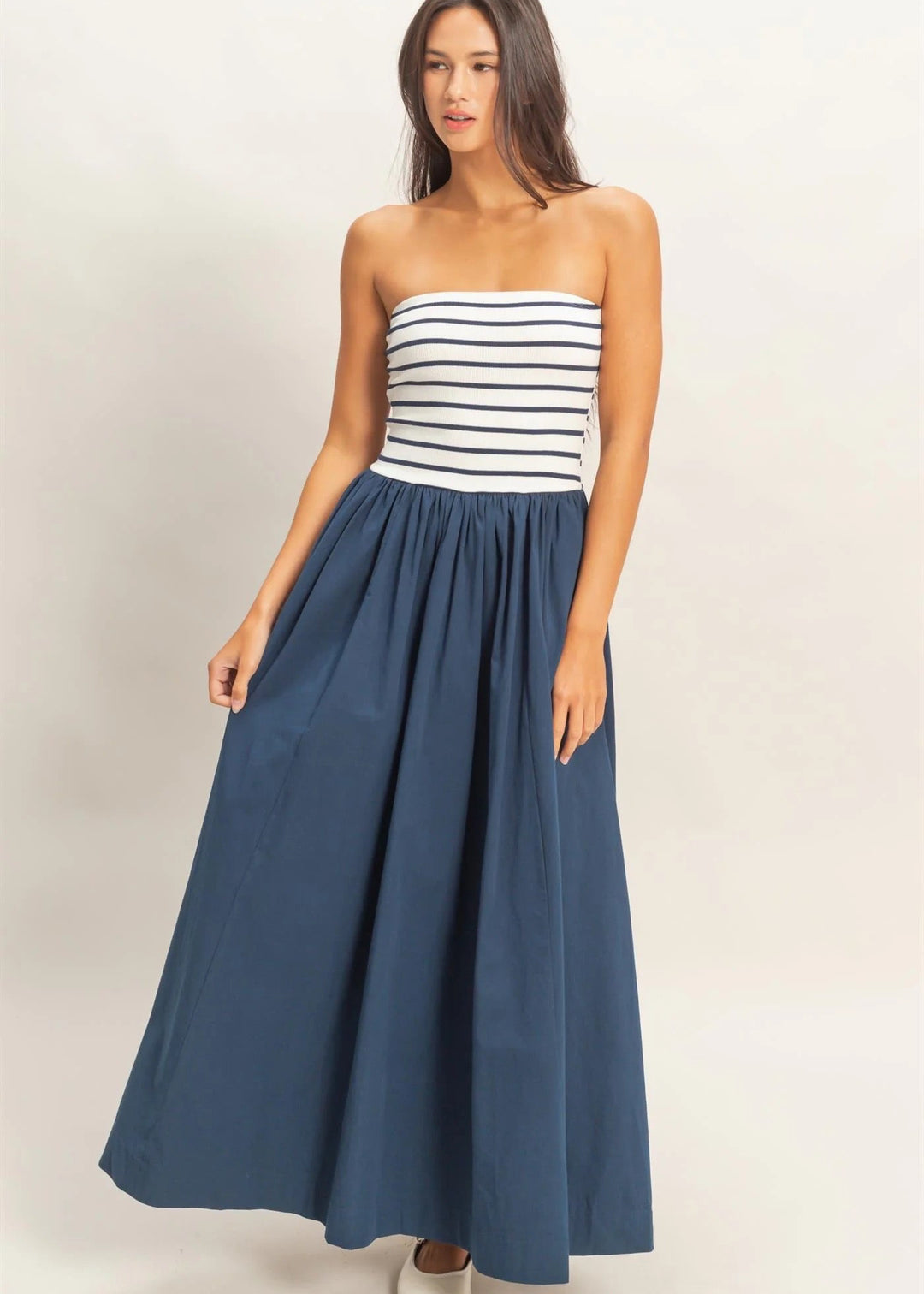 Woman wearing a strapless striped top and long navy skirt on a plain background