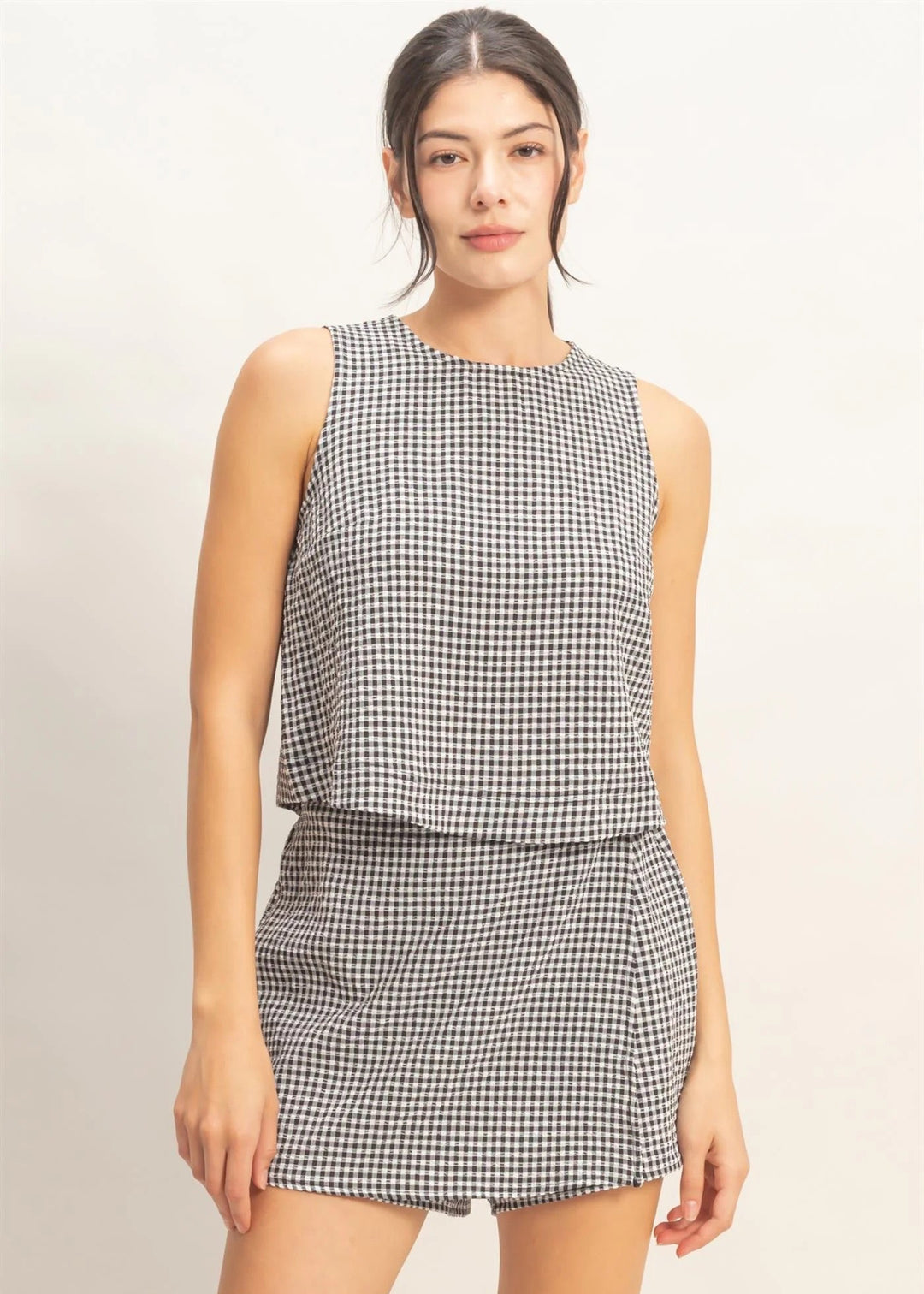 Woman wearing a black and white checkered sleeveless top and skirt on a beige background