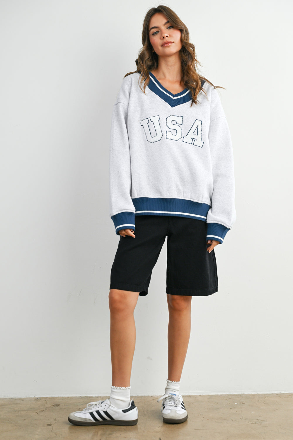 Woman wearing a white 'USA' sweatshirt with blue accents and black shorts on a plain background