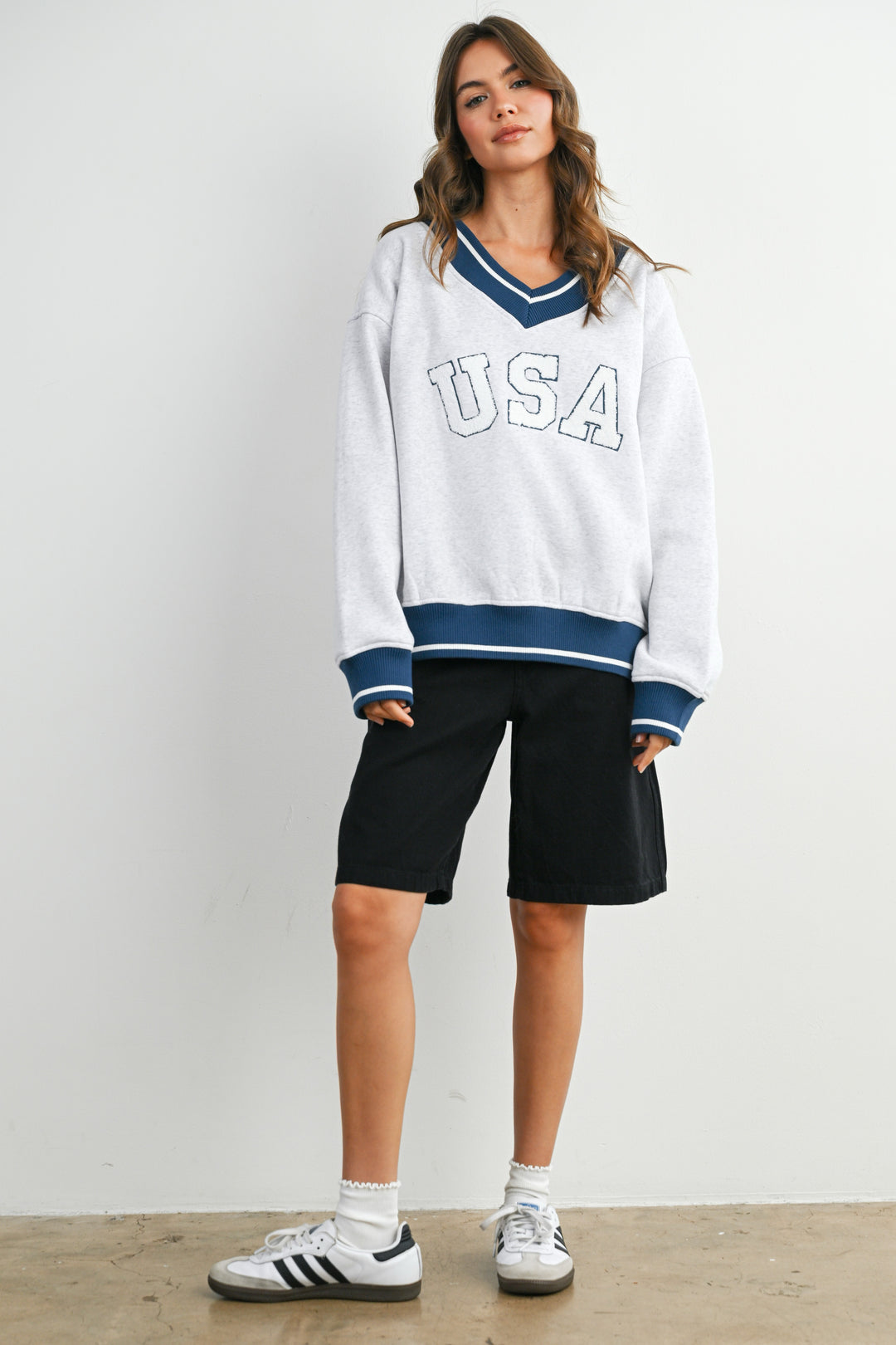 Woman wearing a white 'USA' sweatshirt with blue accents and black shorts on a plain background