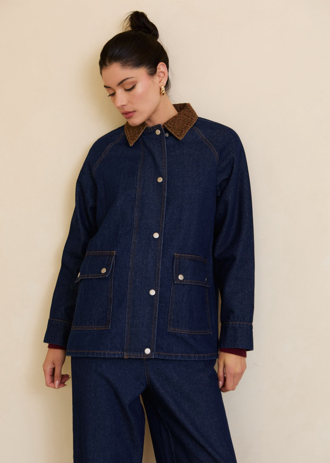 Woman wearing a dark blue denim jacket with brown collar against a beige background