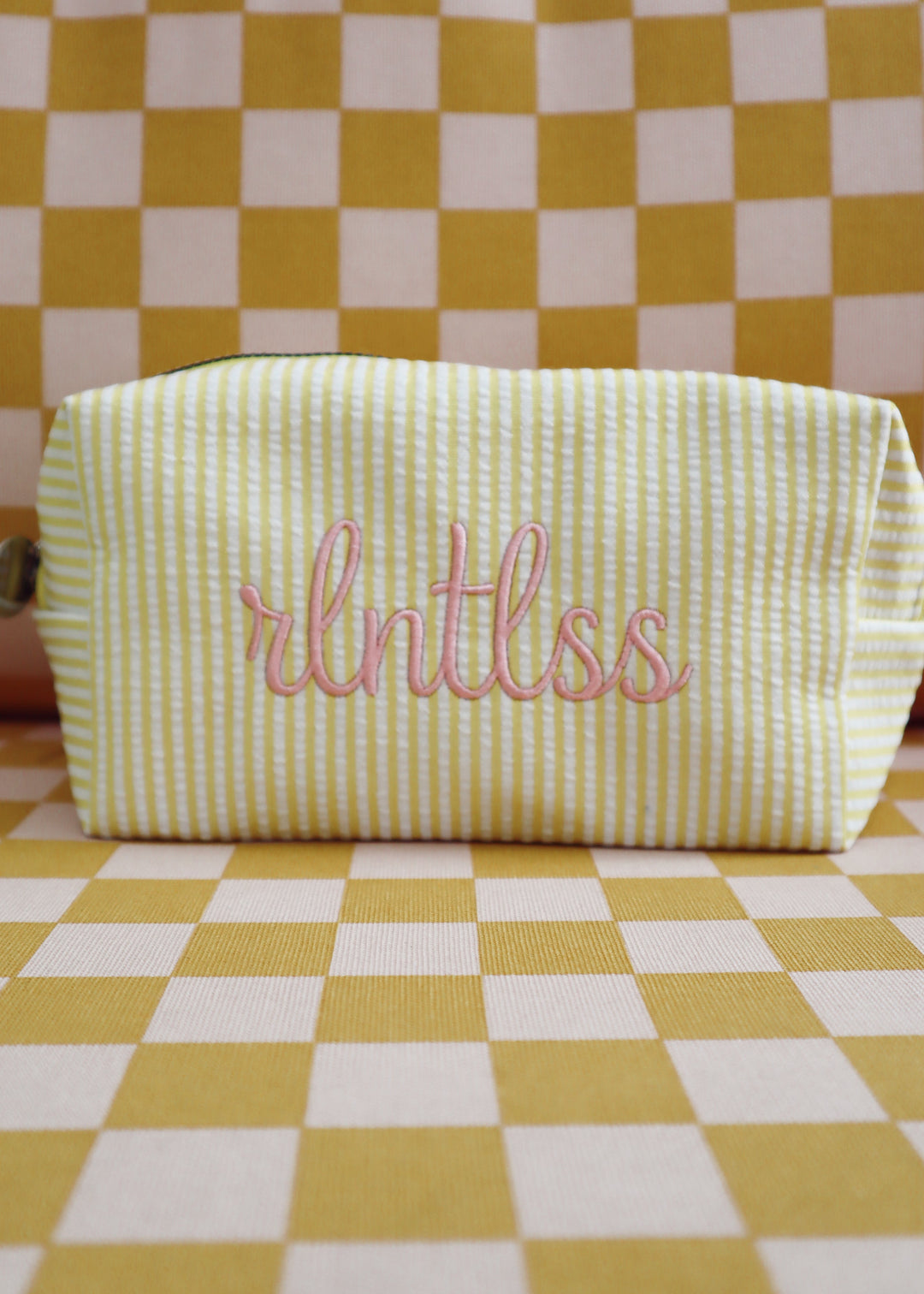 Yellow and white striped pouch with 'rlntlss' embroidery on a yellow and white checkered background