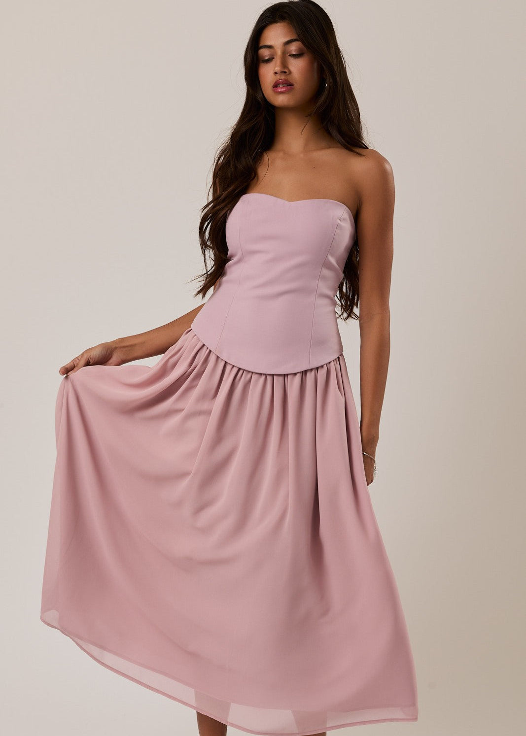 Woman wearing a pink strapless dress against a plain background